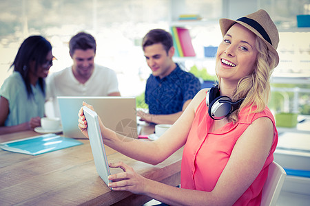 与同事一起工作的有创意的女商务人士微笑职业平板工作室商业头脑听力帽子触摸屏电脑办公室图片