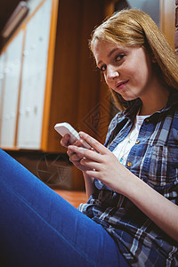 坐在地板上 用智能手机靠墙对着墙的漂亮学生技术微笑知识女性休闲储物柜教育电话短信高等教育图片