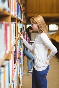在图书馆书架里找书的Blund学生教育女士女性青少年高等教育休闲知识采摘专注文学背景图片