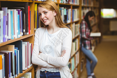 微笑的学生靠在书架的对面青少年高等教育大学生休闲阅读女士混血学校教育女孩图片
