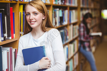 微笑的学生靠在书架的对面女性学校知识女孩青少年高等教育教育图书馆休闲校园图片