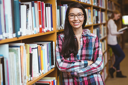 微笑的学生靠在书架的对面大学生知识女孩女士学校大学快乐校园双臂混血图片