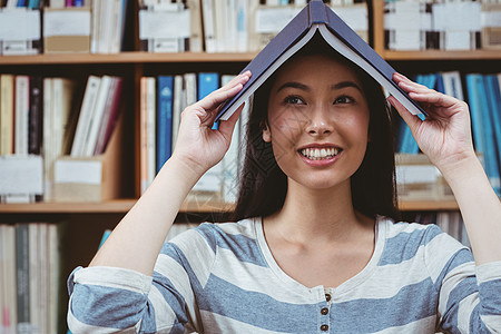 有趣的学生在她头上拿着书校园图书馆混血学校大学教育阅读女性快乐高等教育图片