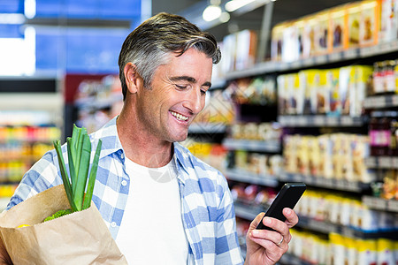 使用智能手机用杂货袋打笑人购物袋男性屏幕电话走道购物零售服装活动消费者图片