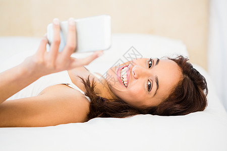 漂亮女人躺在床上时用手机打着她的电话棉被公寓混血枕头短信女性羽绒被睡衣拨号快乐图片