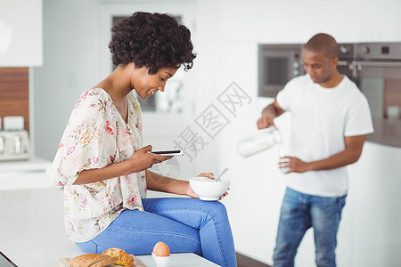 快乐的一对夫妇吃早餐并使用智能手机女士滚刀家庭生活技术屏幕勺子厨房柜台公寓烤箱图片