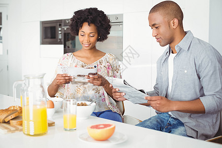 早餐时微笑一对夫妇阅读杂志和文件的喜笑房子柜台男人桌子报纸勺子女性夫妻家庭电饭煲图片