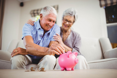 年长男子在小猪银行投硬币住所女性闲暇沙发微笑退休客厅储蓄休闲金融图片