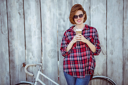 带着咖啡和双臂的笑笑着的嬉皮女人杯子太阳镜女士女性快乐衬衫木头潮人固定器服装图片