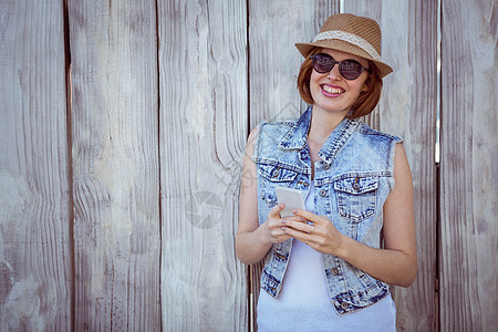 微笑着的嬉笑女人 在她的智能手机上女士快乐潮人阅读眼镜服装屏幕木头外套沟通图片