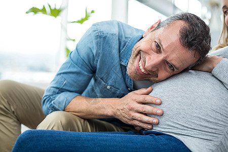男人倾听孕妇的胃部听力男性沙发家庭生活夫妻腹部肚子分娩怀孕孕妇装背景图片