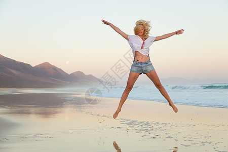 年轻美女在沙滩上跳跃旅行海岸幸福天空日落自由假期旅游青年女孩图片
