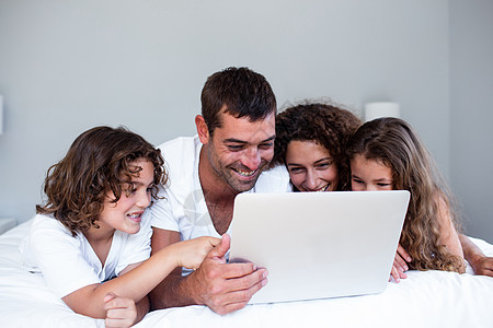 幸福的家庭一起在床上使用笔记本电脑母亲卧室混血说谎男人男性乐趣快乐儿子父亲图片