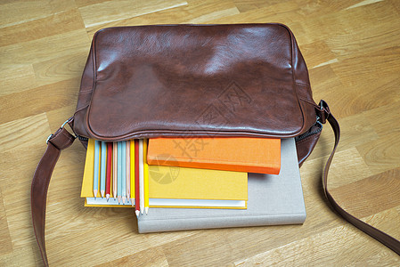 皮革背包中的书本和铅笔手提包学生班级学习字帖褐色学校教育红色橙子背景图片