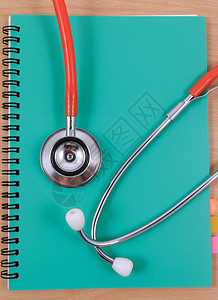红色听诊器躺在薄绿色书上医生乐器办公室知识职业蓝色考试文档记录诊断图片