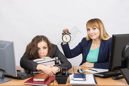 办公室最后有两个女孩 一个带着笑容 拿着钟表 又一个在文件夹上疲倦的谎言图片