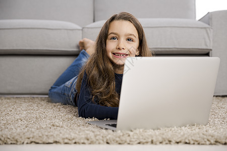 小女孩用笔记本电脑工作微笑说谎娱乐互联网童年技术沙发孩子们地面幸福图片