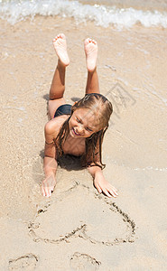 海滩上的小女孩孩子们假期心形乐趣喜悦太阳享受孩子快乐说谎图片