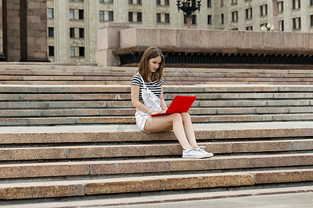 大学附近楼梯上手持笔记本电脑的年轻妇女互联网学生学校柱子闲暇假期建筑女士工作微笑图片