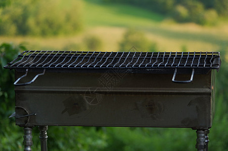 一个空的便携式BBQ烧烤炉 面对新的绿色夏季风景餐具木炭公园网格烧烤野餐工具场景煤球午餐图片