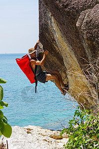 一个坚强而快乐的人 带着小屋和红色的海袋在海上攀登高高的岩石登山者天空旅行男人运动员登山运动力量顶峰勇气图片