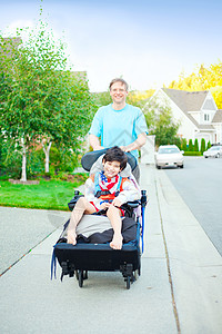 残疾孩子父亲将10岁残疾的儿子推到户外轮椅上医疗父母脑瘫机动性帮助人行道微笑少数民族白色乐趣背景