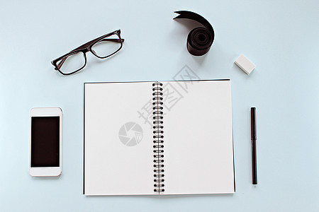以空白笔记本 眼眼镜 智能电话 彩带和蓝背景办公文具为顶层工作空间台视图 创造性平板套装设计图片