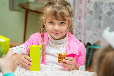 早餐包装女孩在幼儿园的桌子边喝果汁 吃饼干 吃饼干背景