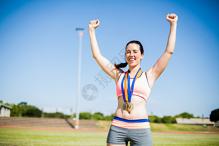 兴奋的女运动员 脖子上戴着金牌胜利勋章喜悦晴天运动丝带竞赛能力快乐体育场图片