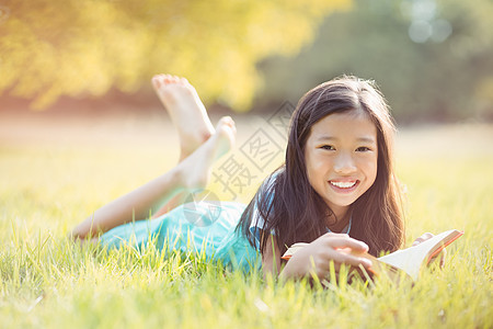 躺在草地上微笑的女孩和公园阅读书的肖像图片