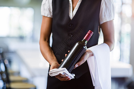 中间的女服务员拿着一瓶红酒和一条毛巾饮料女性服务女士茶点餐厅工人酒精酒瓶酒店图片
