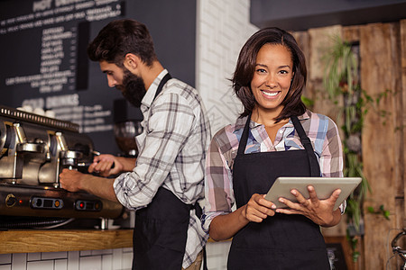 使用平板电脑和咖啡机服务员的服务员滚动制服女士咖啡微笑女性工作衬衫马甲男性图片