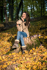 女孩坐在树桩上情感咖啡森林树叶女儿叶子公园微笑黑发牛仔裤图片