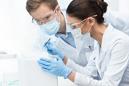 戴防护眼镜和面具的年轻男女科学家做实验化学家化学品伙伴科学实验室手套合作安全化学同事图片