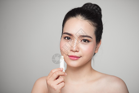 亚裔女性在灰色背景上施用卫生唇膏皮肤治疗口红护理化妆品嘴唇女士图片