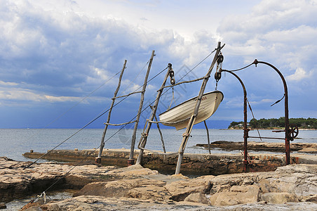 悬挂在传统起重机上的小型渔船假期天空日落海洋支撑收成蓝色海滩海岸紫色图片