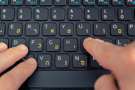 用希伯来语和英语字母在键盘打字的人桌子商业行动成人手指冲浪学生教育互联网人士图片