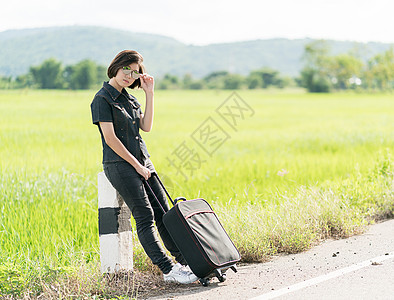 在公路上搭便车载行李的妇女假期游客案件短发太阳镜天空女性自由冒险女士背景