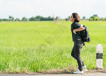 带着背包搭便车走在路边的女人青少年女孩牛仔裤旅游场地天空短发游客太阳镜农村图片