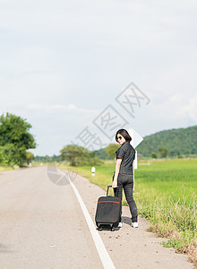 在公路上搭便车载行李的妇女女性假期国家太阳镜旅游远足路线天空自由农村背景