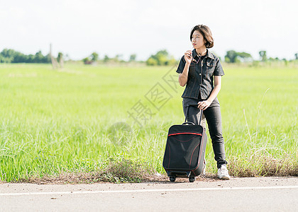 在公路上搭便车载行李的妇女牛仔裤自由国家农村游客青少年案件天空短发假期图片