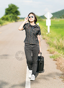 在公路上搭便车载行李的妇女假期天空路线自由案件女孩游客牛仔裤场地旅游图片