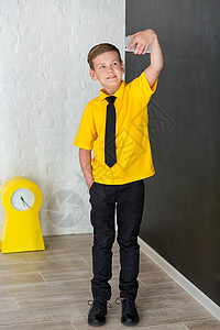 穿着黄色 T 恤领带和时尚靴子的可爱帅气男学生休闲装站在黑板上 上面有数字 拿着智能手机和微笑愿望粉笔课堂男生学习眼镜孩子教学男图片
