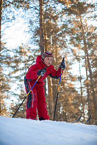 穿红衣服男孩穿红衣服的男孩在松树林里滑雪假期森林童年滑雪者闲暇孩子们季节喜悦公园运动背景