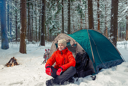 坐在冬季森林中帐篷附近的放松的旅游女游客图片