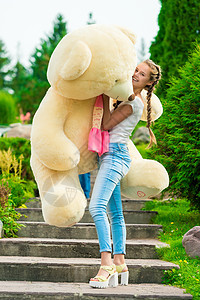 快乐的年轻女孩 在公园里摆着一只大泰迪熊图片