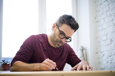 年轻设计师 在Bright工作室的Wooden桌上用铅笔绘制画图黑发男人工具工匠草图男性蓝图学习创造力职业背景图片