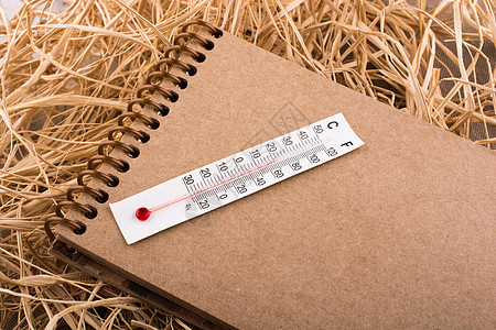 棕色笔记本上的温度计 在稻草背景上温度工具指标气候测量白色乐器图片