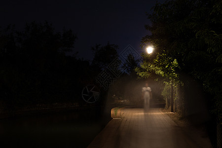 晚上人人在黑暗的街道上行走的双重曝光夜景被路灯照亮 公园道路上逐渐远去的男性剪影 沿着城市河流运动模糊的人物形象路人犯罪开膛手胡同照明背景