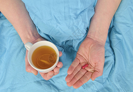 发烧的病人喝杯温茶 吃药 流感季节 病人的手拿着药丸和一杯热茶躺在床上 生病的白种人在家的特写镜头身体就寝治疗时间一部分感染疾病图片